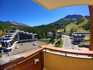A view from a balcony overlooking a parking area with buildings and a road leading to a mountain. - 50m from ski slopes, 5th floor, view ski slopes, balcony, ski locker, 40m², Vars (Vars)