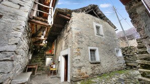 Ein Steinhaus mit einer Holztreppe, einem Tisch mit Stühlen und einem Fenster.