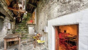 Eine rustikale Steintreppe führt zu einem Essbereich mit Schachbrettboden und einem Holztisch mit Stühlen.
