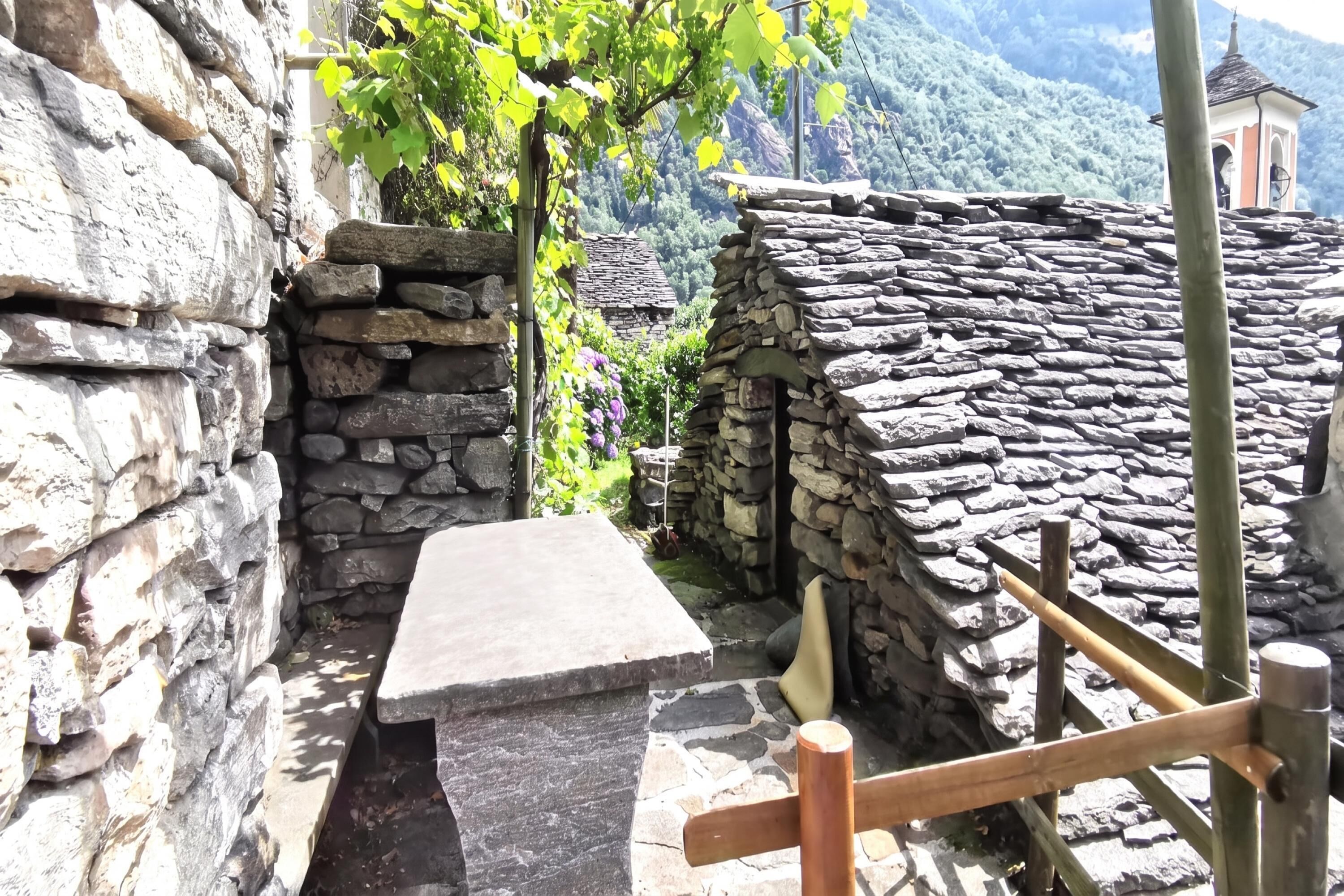 A stone bench in a narrow alleyway, with a stone wall on one side and a stone building on the other.