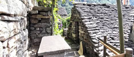 A stone bench in a narrow alleyway, with a stone wall on one side and a stone building on the other.