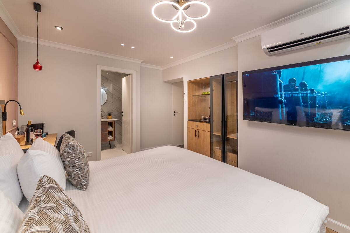 A modern bedroom with a large bed, a TV mounted on the wall, and a wardrobe.