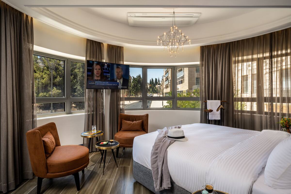 A hotel room with a large bed, two armchairs, a TV, and a view of the outdoors.