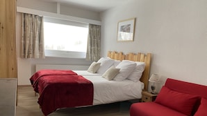 A bedroom with two beds, a wooden headboard, a red sofa, and a bedside table with a lamp.