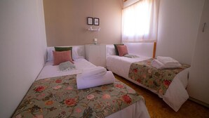 Habitación de hotel con dos camas individuales, cada una con cubrecama floral y ropa blanca. Hay un mueble pequeño y un cuadro en la pared.
