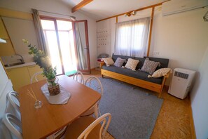 Una sala de estar acogedora con un sofá, una mesa de comedor con sillas, una zona de cocina y un gran ventanal con cortinas.