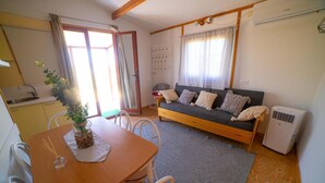 Ein gemütliches Wohnzimmer mit Sofa, einem Esstisch mit Stühlen, einer Küchenzeile und einem großen Fenster mit Vorhängen.