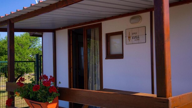 A wooden structure with a covered porch, a window, and a plaque with text. - Las Casitas de Guadamur.(Domus Wamba) (Guadamur)