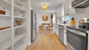 A modern kitchen with white cabinetry, a wooden dining table, and a hanging light fixture.