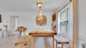 A dining area with a wooden table, benches, a hanging light fixture, and a window with curtains.