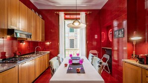 A compact kitchen with wooden cabinets, a dining table set for four, and a view through a window to an outdoor area. - Billie's Flat RED - art & design apt in Verona historic centre (Verona)