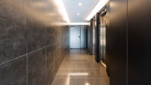 A modern hallway with dark tiled walls and a shiny floor, leading to an elevator and a door at the end. - Camões Downtown with Parking (Porto)