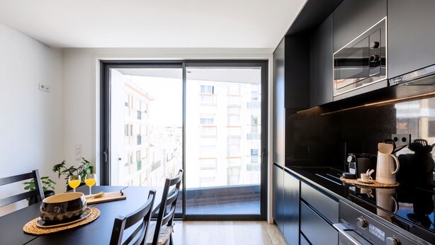 A modern kitchen with a large window, a dining table, and a view of buildings outside. - Camões Downtown with Parking (Porto)