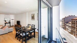 A modern apartment with a dining area, a sofa, and a large window overlooking a street. - Camões Downtown with Parking (Porto)