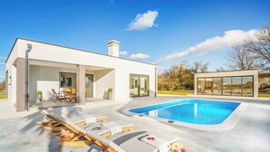 Ein modernes Haus mit Schwimmbad, Sitzgelegenheiten im Freien und einer Terrassenfläche.