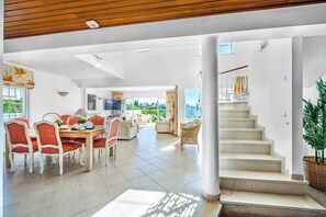 Amplia sala de estar con una mesa de comedor, sillas y una escalera que lleva a un piso superior.