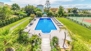 Ein Swimmingpool, umgeben von einem gepflegten Garten, mit einem Tennisplatz im Hintergrund.