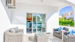 Ein moderner Außenbereich mit Rattanmöbeln, einer Glastür, die auf eine Terrasse führt, und einer an der Wand montierten Klimaanlage.