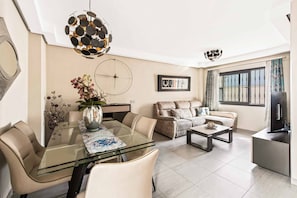 Una sala de estar moderna con una mesa de comedor de vidrio, un sofá color beige y un televisor.