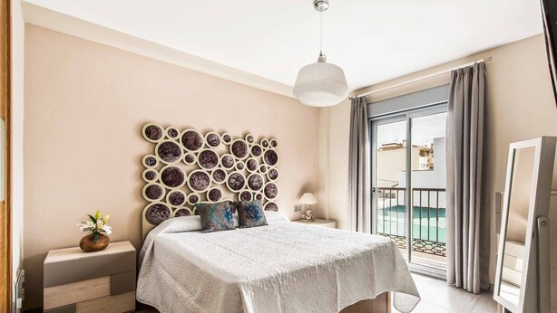 Une chambre dotée d’un grand lit, d’une tête de lit décorative, d’une table de chevet avec une lampe et donnant sur le balcon extérieur.