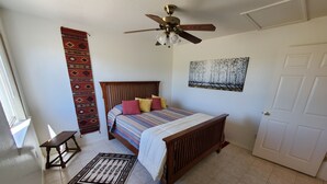 Une chambre avec un lit en bois, un ventilateur de plafond, un tapis à motifs et une porte.