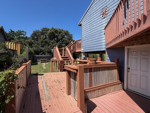A wooden deck with a staircase leading to a blue building with a wheel emblem. - SeaClusion II:  Two-story vacation rental duplex (Ocracoke)