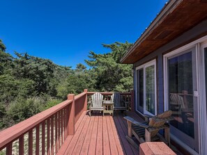 A wooden deck with a railing, a covered area with a table and chairs, and a view of trees and sky.