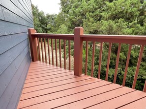 A wooden deck with a red railing, surrounded by dense green trees.