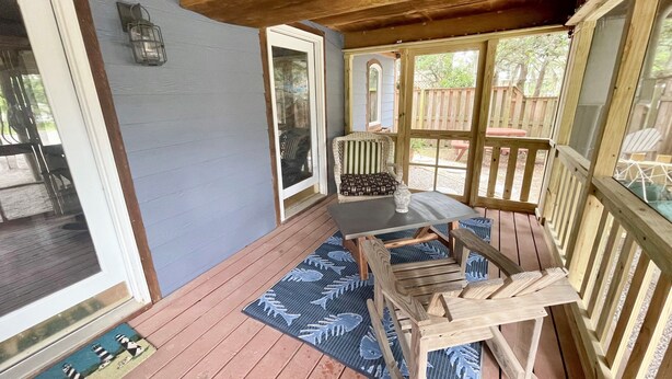 A covered porch with a wooden bench, a table with a vase, and a view of the backyard. - SeaClusion I:  Two-story vacation rental duplex (Ocracoke)