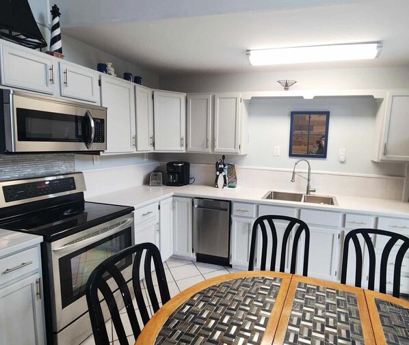 Una cocina compacta con armarios blancos, microondas, estufa, lavavajillas y pileta. En el centro, hay una mesa redonda con sillas.