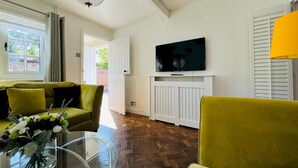 Ein Wohnzimmer mit einer Couch, einem Glastisch, einem an einer weißen Wand montierten Fernseher und einer Chandelier.