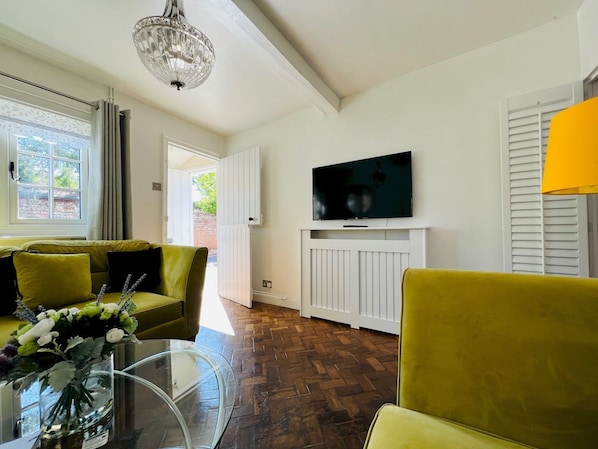 A living room with a sofa, a glass coffee table, a TV mounted on a white wall, and a chandelier.
