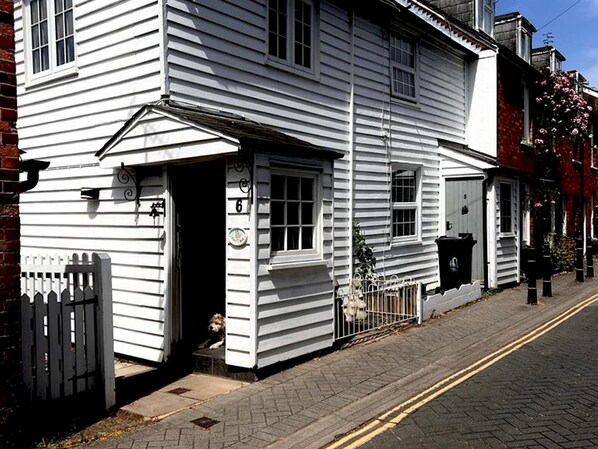 A white two-story house with a front porch, a small dog visible through the open door, and a mailbox on the sidewalk. - Bridewell Cottage in the heart of Tenterden - Pass the Keys (Tenterden)