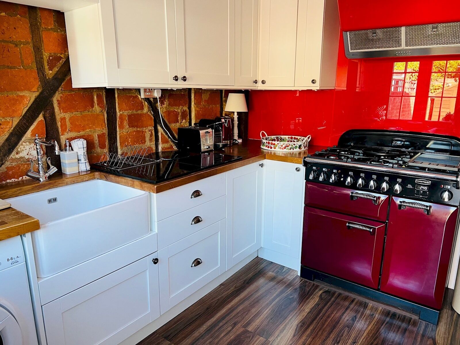 Une cuisine avec des meubles blancs, une cuisinière à gaz rouge et un mur en briques.