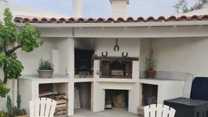 Un patio al aire libre con dos sillas Adirondack blancas, una mesa redonda pequeña y una parrilla.