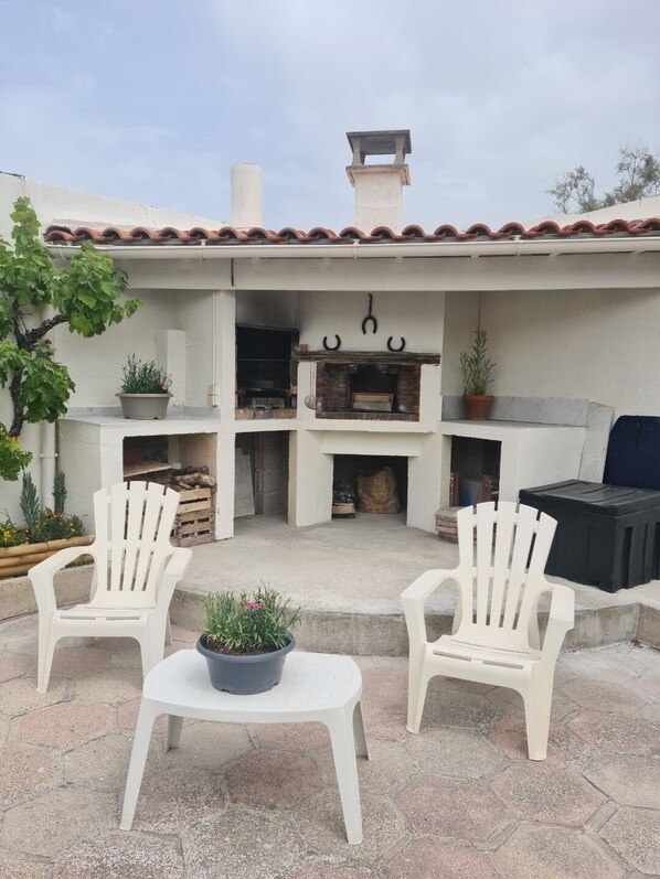 An outdoor patio with two white Adirondack chairs, a small round table, and a grill.