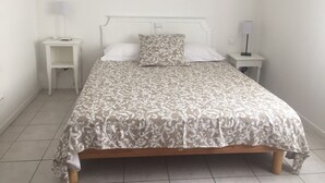 Habitación individual con ropa de cama estampada, cabecera blanca, dos mesitas de noche con lámparas y piso de baldosas.