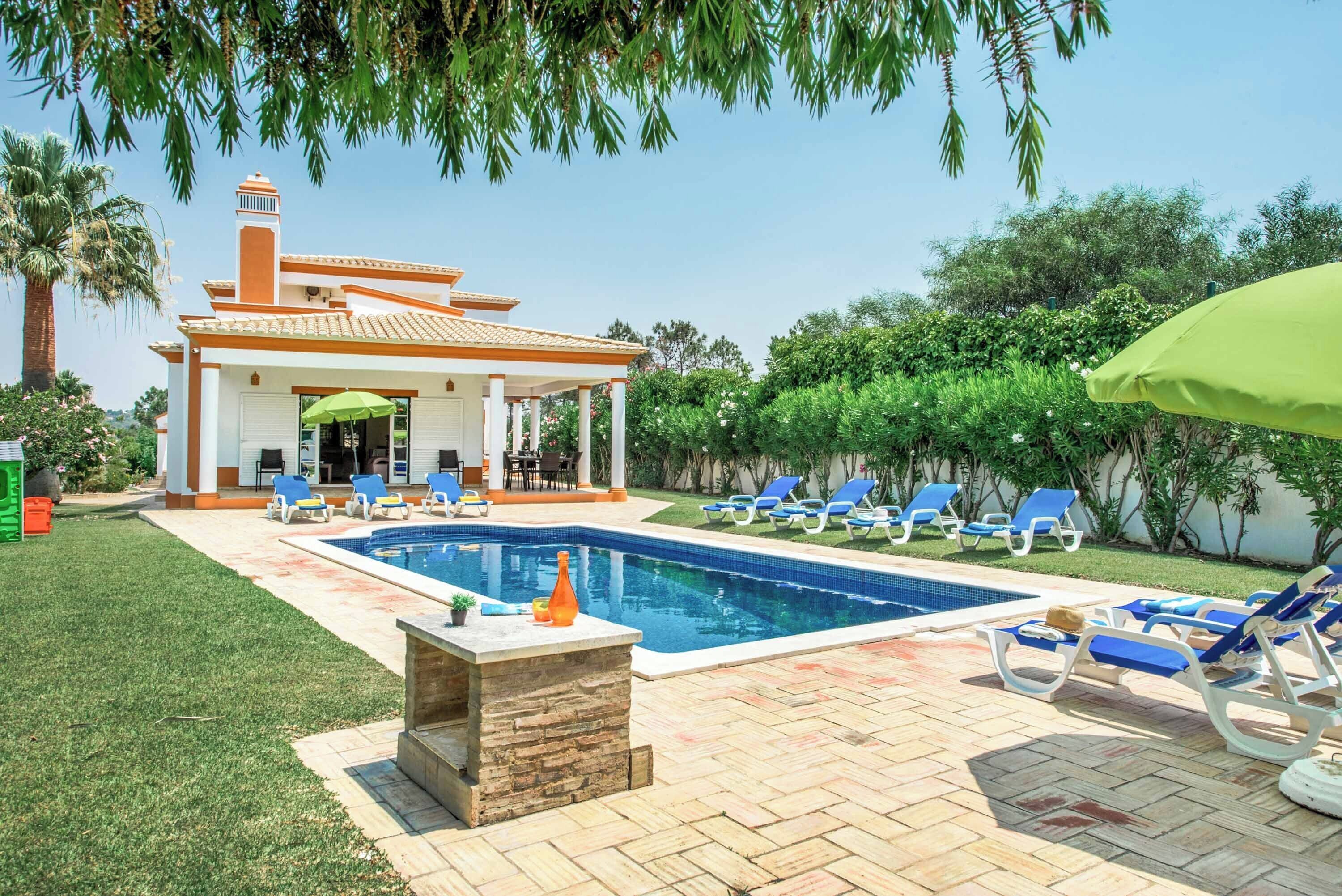 A swimming pool with lounge chairs, a covered patio, and a house with a chimney.