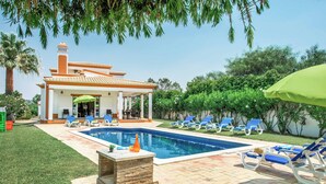 Una piscina con sillas de descanso, un porche cubierto y una casa con chimenea.