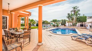 Un espace extérieur avec une piscine, comprenant une table et des chaises pour les repas, ainsi que des fauteuils de relaxation disposés autour de la piscine.