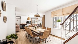 A spacious dining area with a long table, wicker chairs, and a modern chandelier.