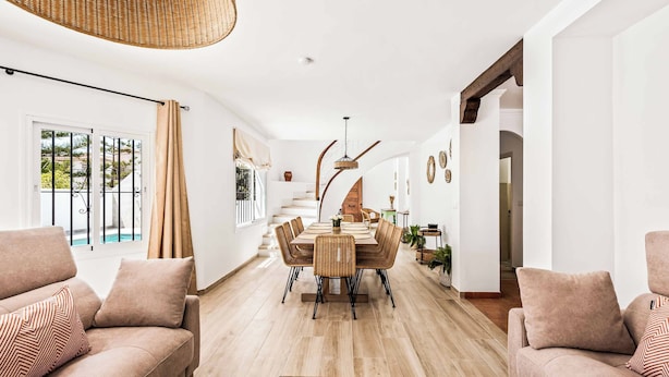 A spacious living room with a dining area, a staircase, and a view of a pool.