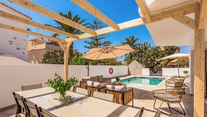 A covered outdoor patio with a pool, wooden furniture, and a table with chairs.