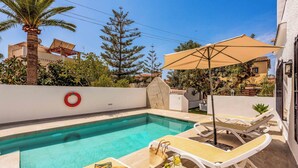A pool area with lounge chairs, a table with a drink tray, and a life ring on the wall.