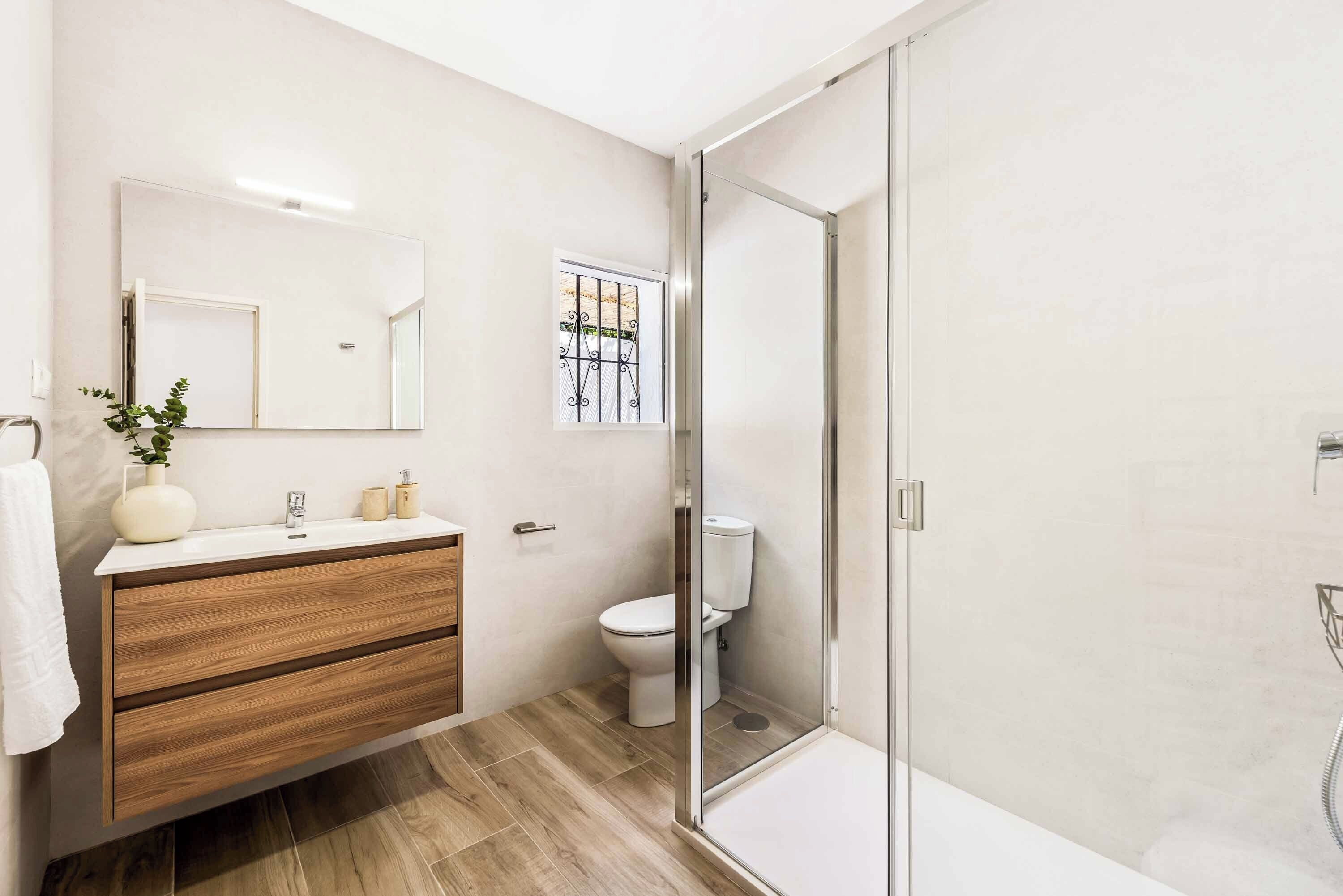 A modern bathroom with a wooden vanity, a glass shower enclosure, and a toilet.