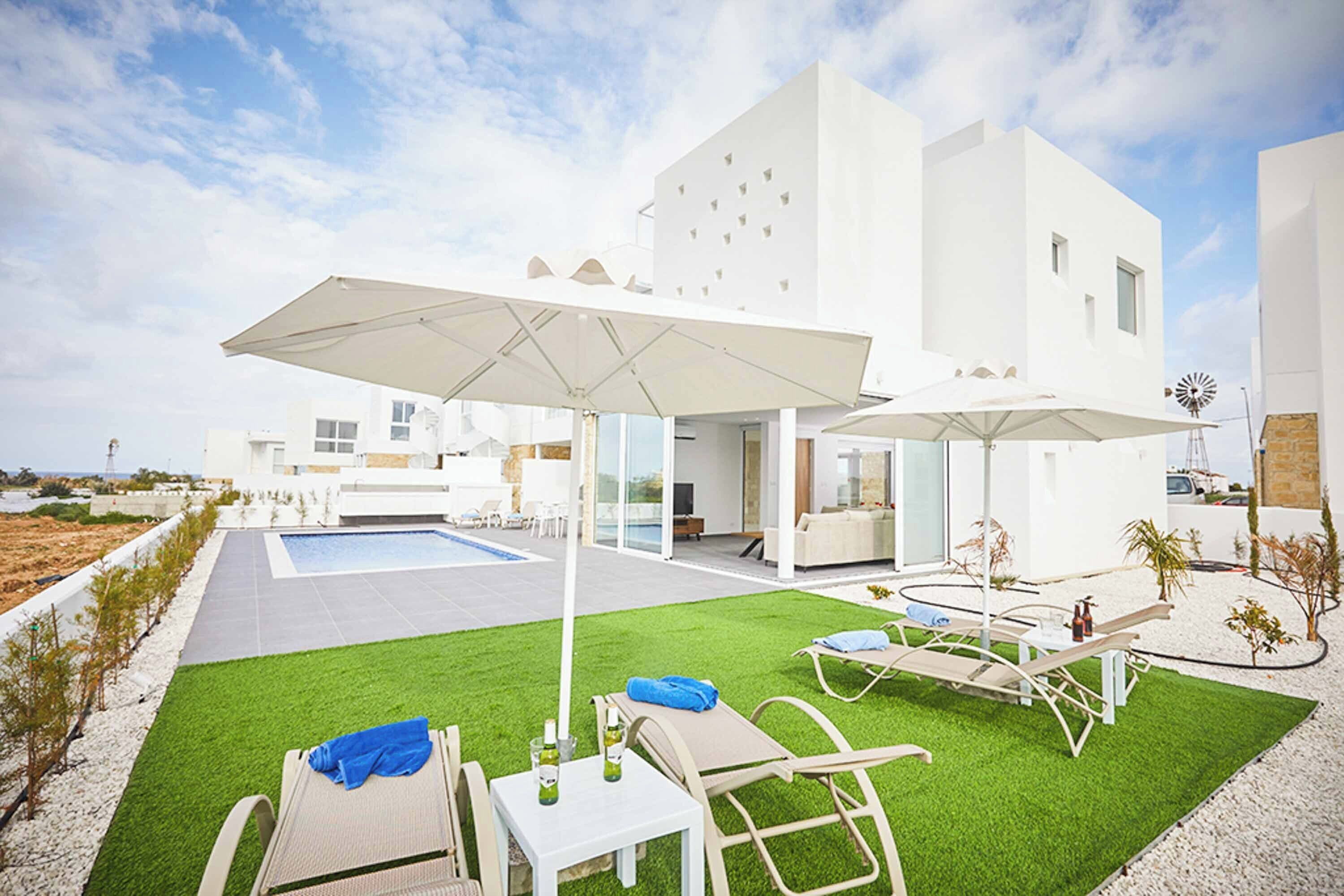 A modern outdoor patio with a pool, lounge chairs, and umbrellas.