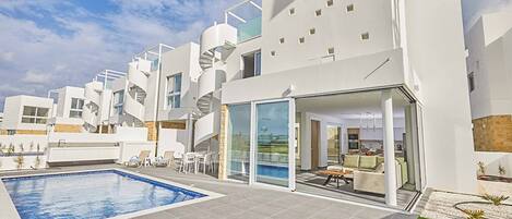 Un edifici residencial modern amb piscina, zona d'estar a l'aire lliure i espai de vivenda amb envans de vidre.