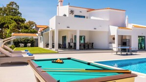 Ein Poolbereich mit Billardtisch, Liegestühlen und einem modernen Haus mit Ziegeldach.