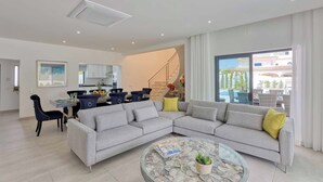 Ein modernes Wohnzimmer mit einer grauen Eckcouch, einem Glastisch und einem Essbereich mit Stühlen und Tisch.