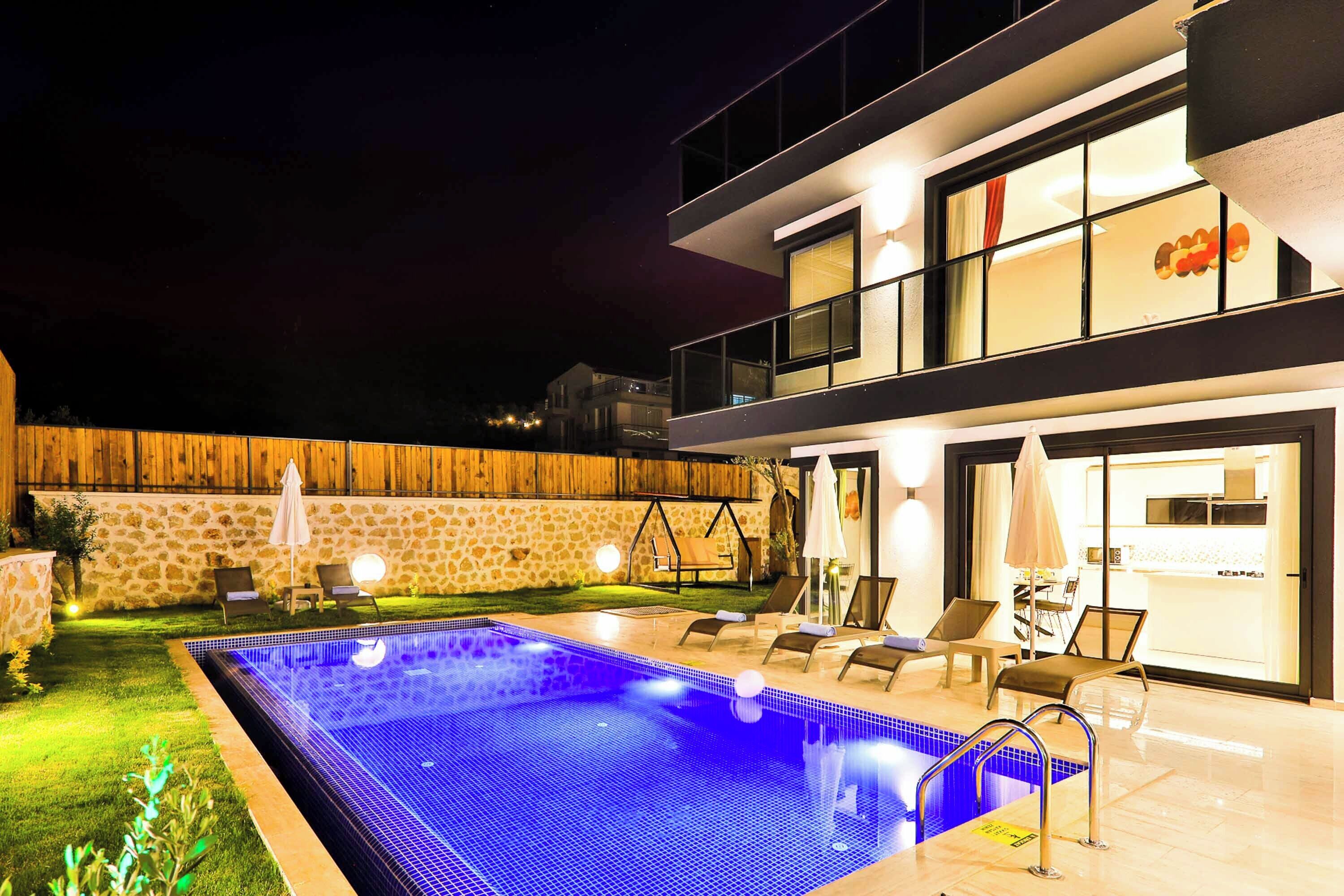 A modern two-story house with a swimming pool, outdoor seating, and a stone wall.